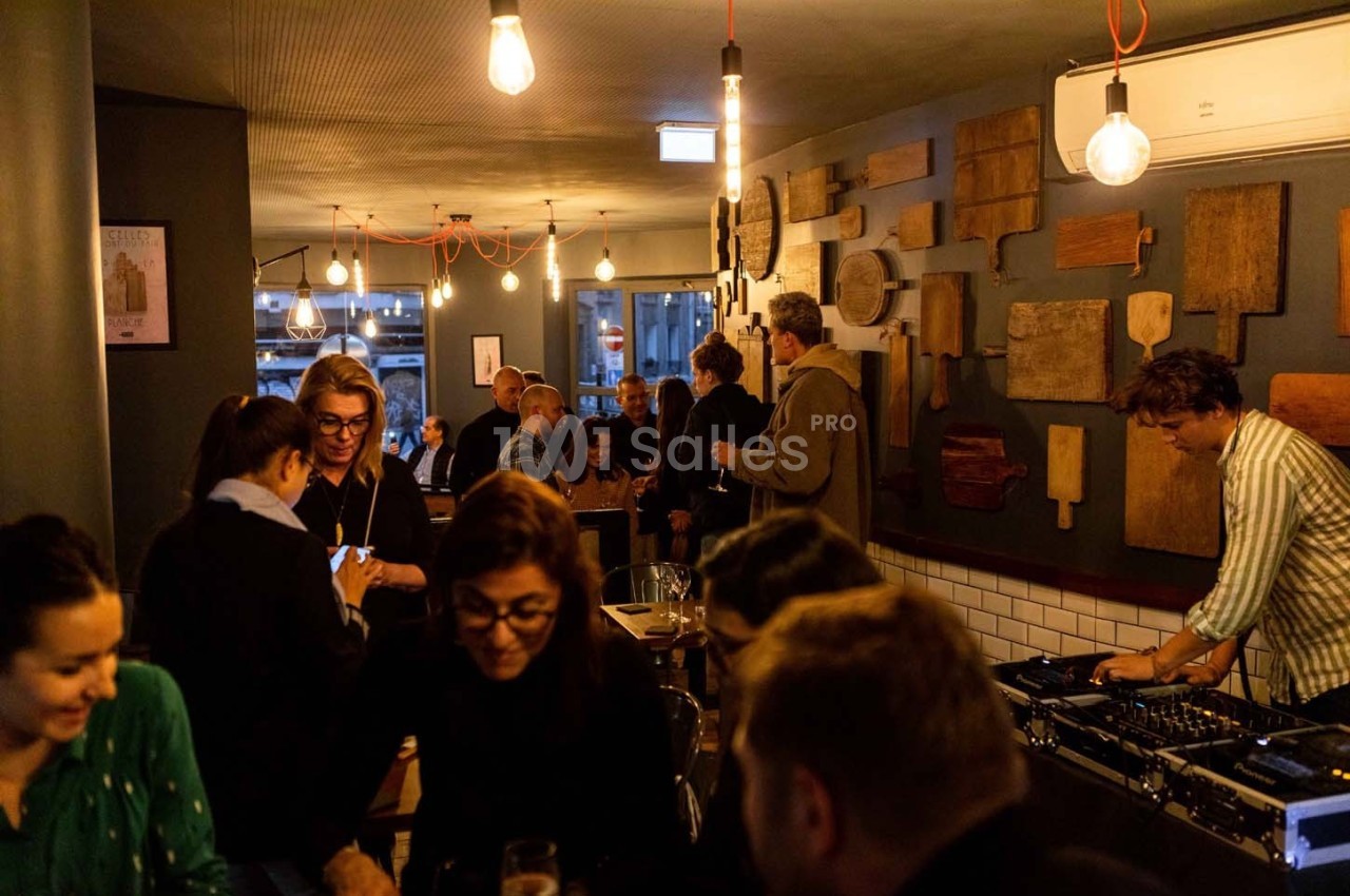 Des personnes discutent et se détendent dans un bar chaleureux, avec un DJ jouant de la musique en arrière-plan.