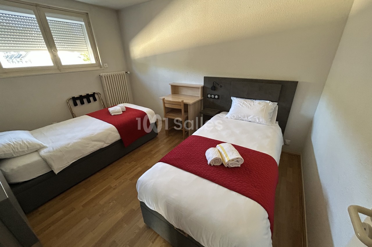 Deux lits simples avec couettes blanches et plaids rouges dans une chambre lumineuse au sol en parquet.