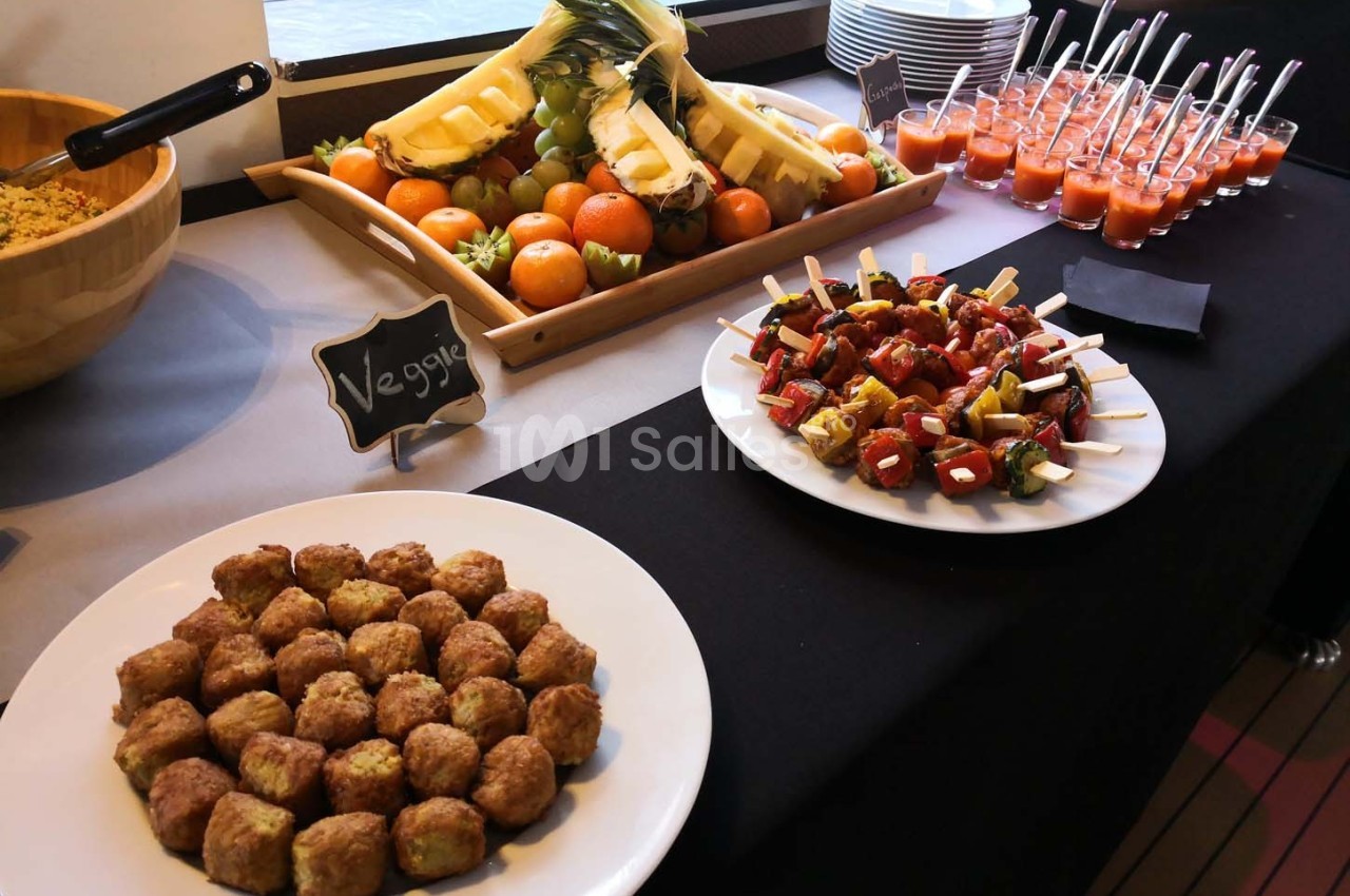 Buffet avec brochettes végétariennes, boulettes, fruits frais et verrines de soupe sur une table noire.
