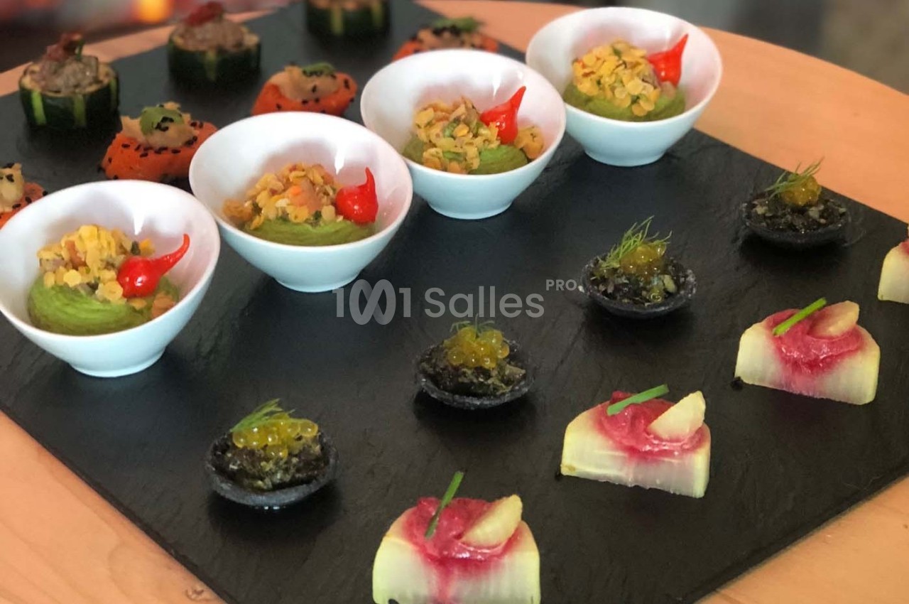 Assortiment de bouchées gastronomiques présentées sur une ardoise, incluant verrines, tartelettes et amuse-bouches colorés.