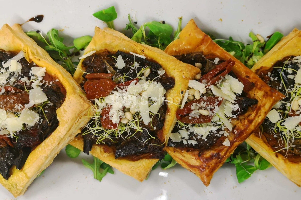 Tartes feuilletées garnies de champignons, tomates séchées, pousses et copeaux de fromage sur un lit de verdure.