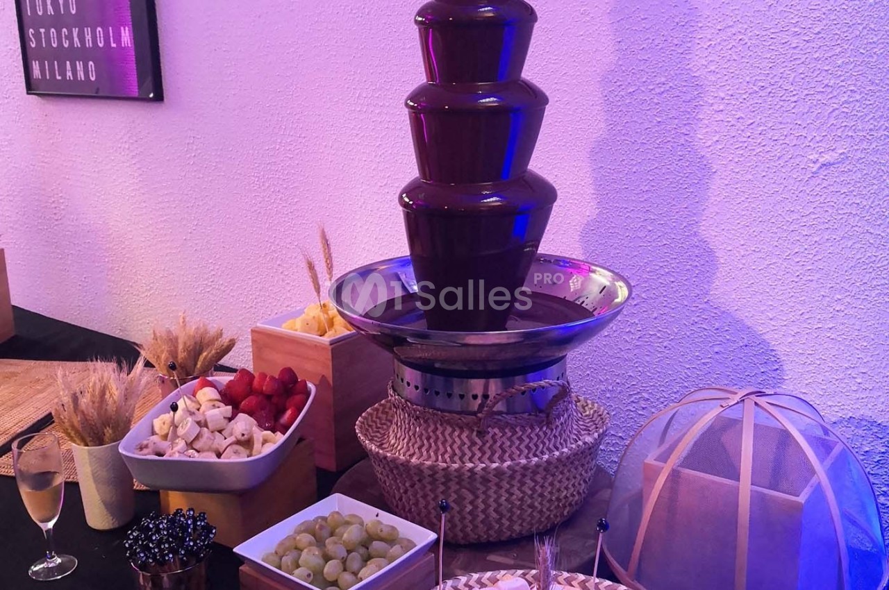 Fontaine à chocolat entourée de fruits frais (raisins, fraises, bananes) et de brochettes pour tremper.