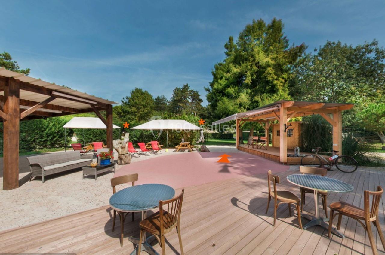 Terrasse extérieure avec tables, chaises, parasols, pergola en bois et végétation en arrière-plan.