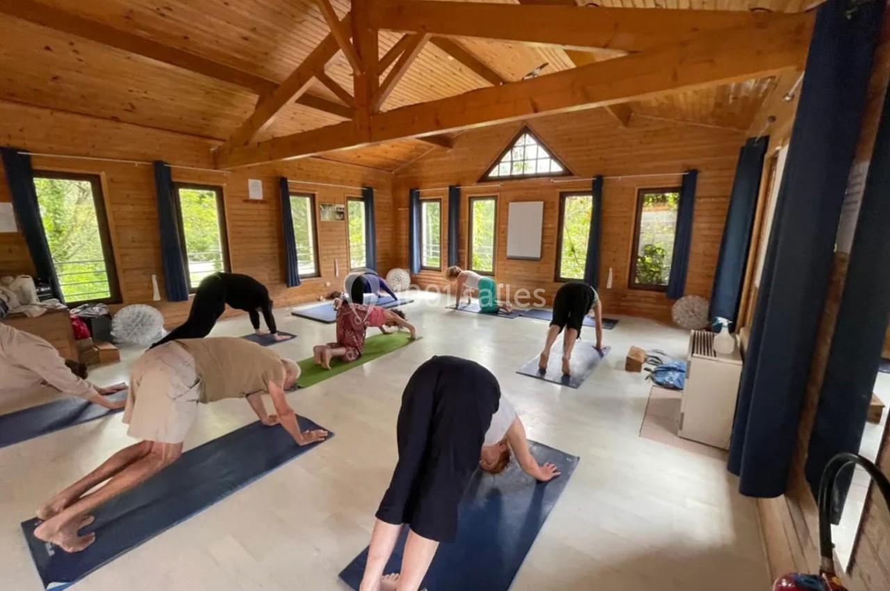 Personnes pratiquant le yoga dans une salle en bois lumineuse, chacune sur un tapis, en position chien tête en bas.