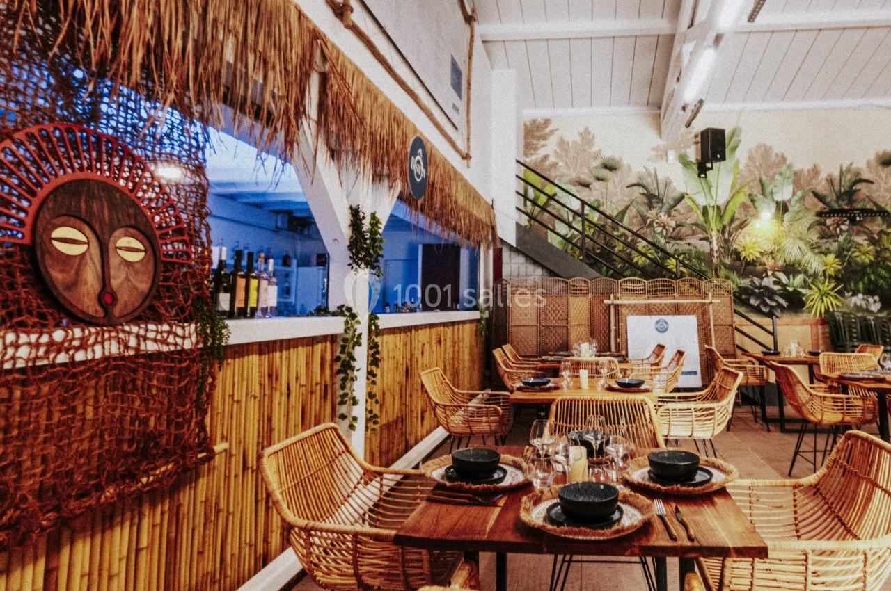 Salle de restaurant décorée de bambou et d'éléments exotiques, avec des tables dressées et des chaises en rotin.