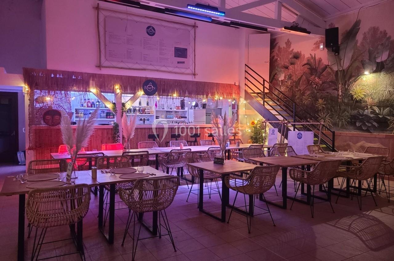 Salle de restaurant décorée avec des tables en bois, chaises en rotin et éclairage tamisé, ambiance chaleureuse.
