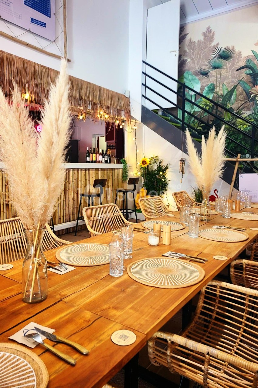 Salle de restaurant décorée avec des meubles en rotin, des vases de pampas et un mur végétal en arrière-plan.