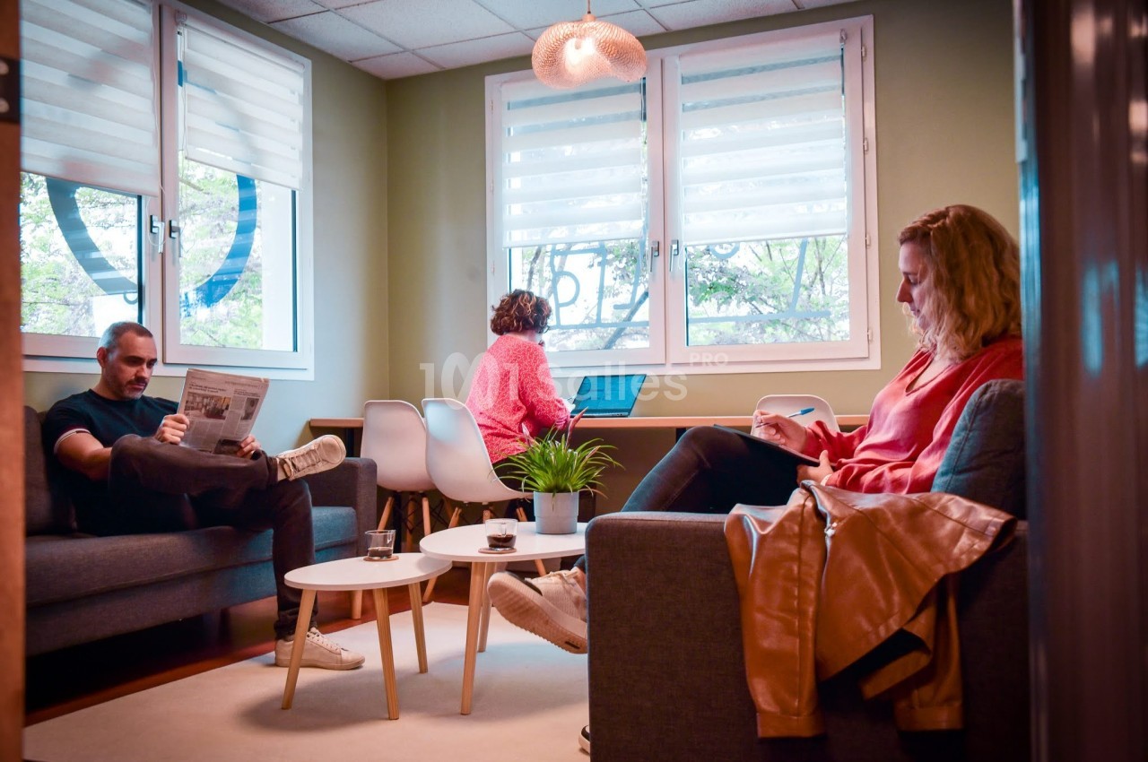 Trois personnes assises dans un espace de détente lumineux, lisant ou travaillant sur un ordinateur portable.