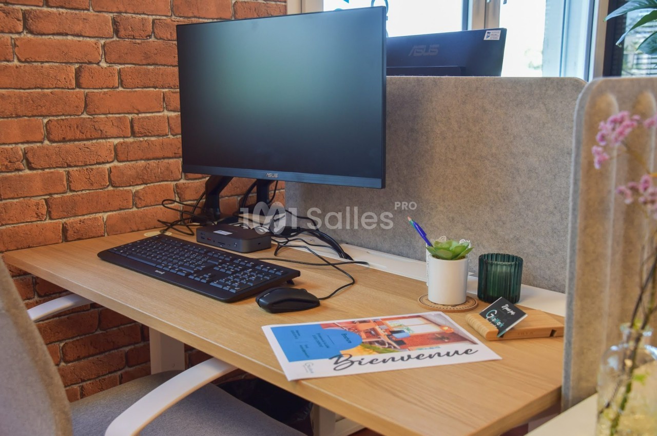 Bureau avec écran d'ordinateur, clavier, souris, plante, bougie et documents posés sur une table en bois clair.