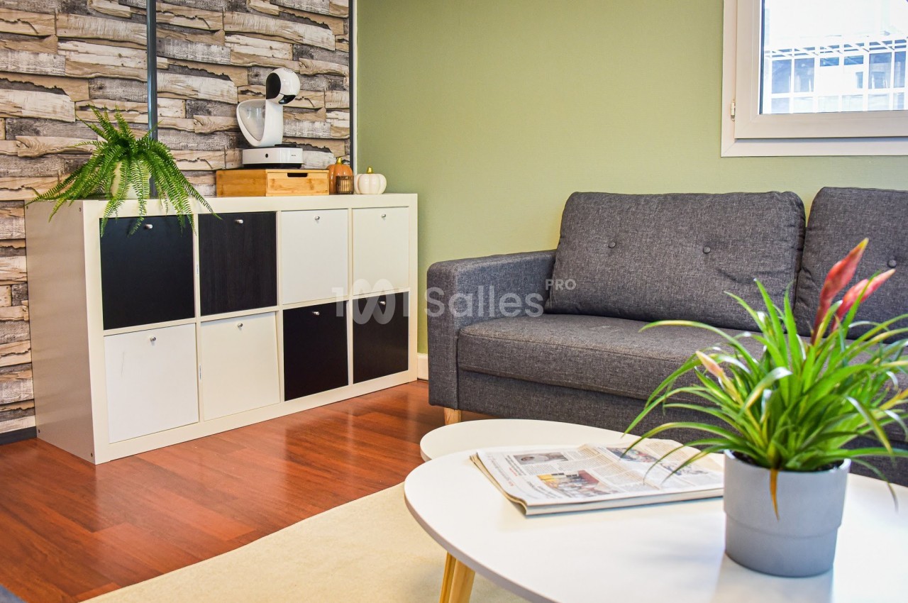 Salon avec canapé gris, table basse blanche, étagère à casiers, plantes vertes et mur à motif bois.