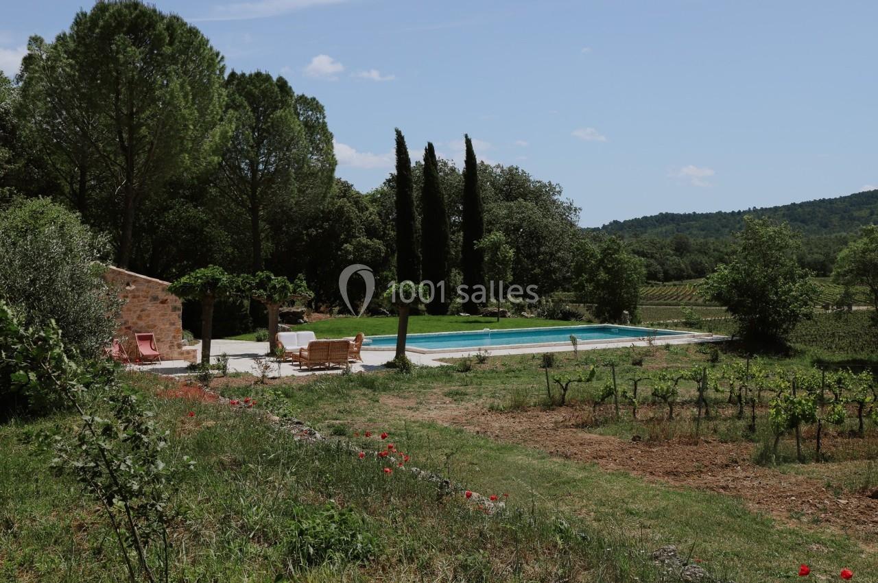 Piscine extérieure entourée de végétation, avec des chaises longues et une maison en pierre à proximité.