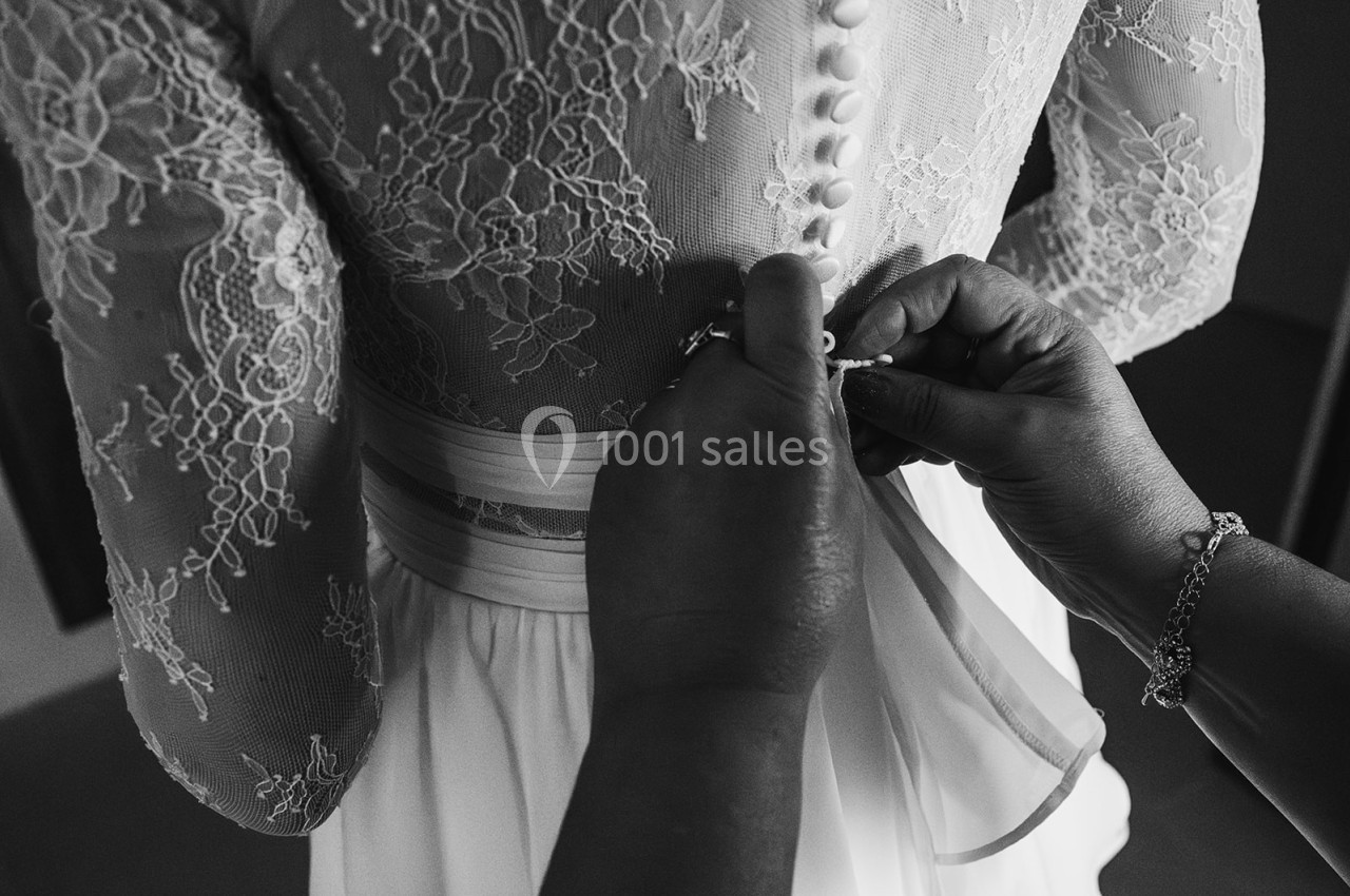 Une personne attache les boutons dans le dos d'une robe de mariée en dentelle.