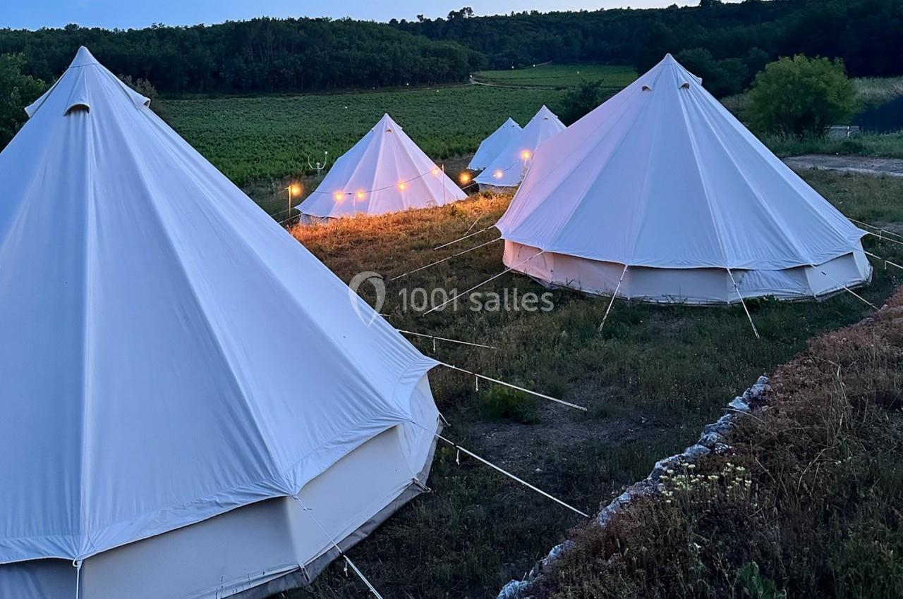 Tentes blanches en forme de cloche installées dans un champ au crépuscule, éclairées par des guirlandes lumineuses.