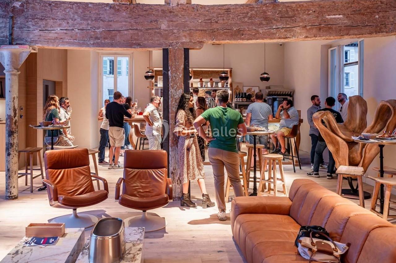 Des personnes discutent et se détendent dans un espace lumineux avec des fauteuils en cuir et un bar en arrière-plan.