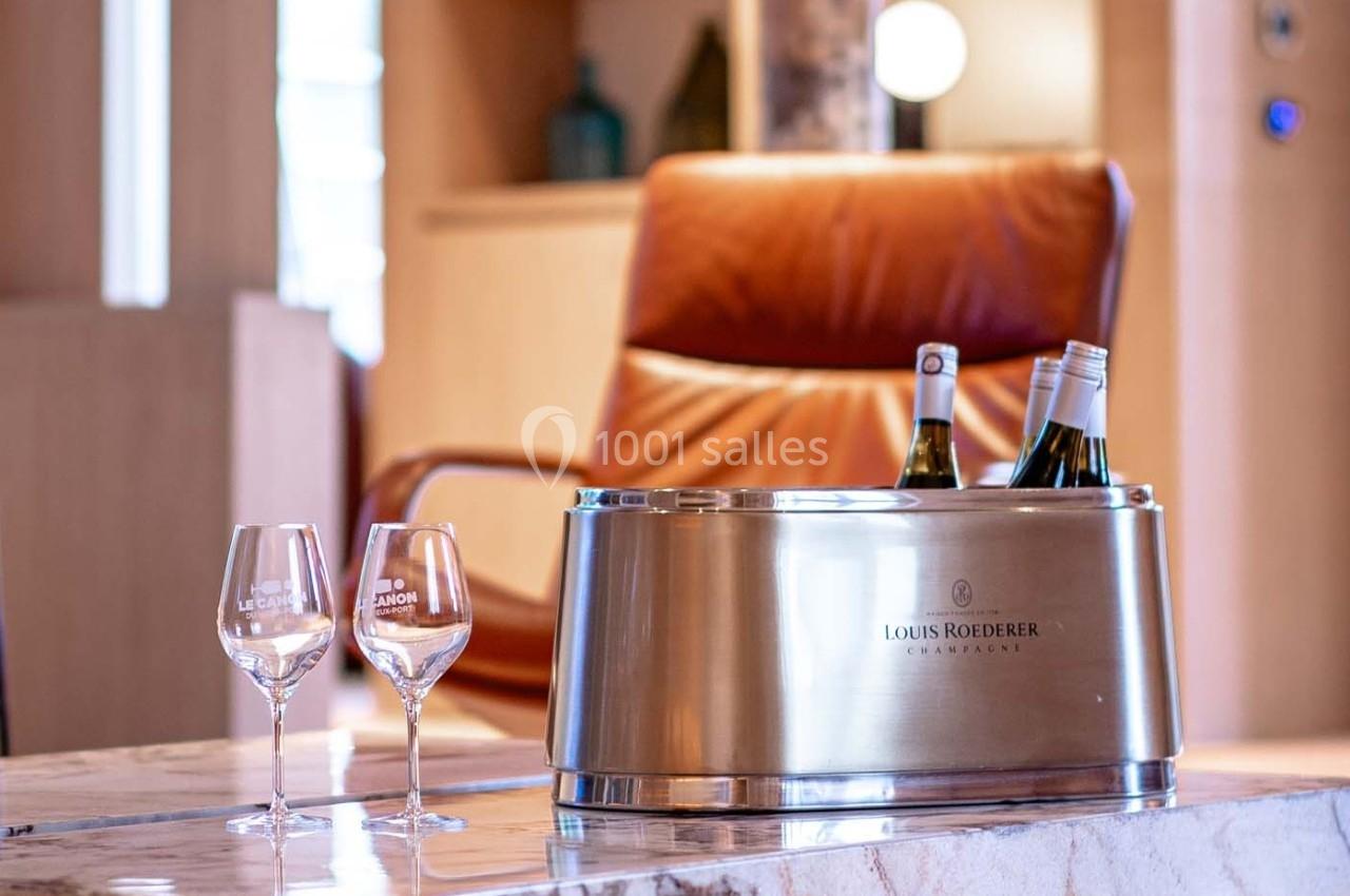 Seau à champagne avec bouteilles et deux verres sur une table en marbre, fauteuil en cuir en arrière-plan.