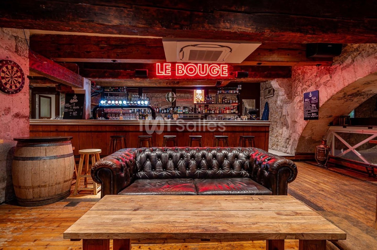 Canapé en cuir devant une table en bois dans un bar à l'ambiance rustique avec un néon rouge ’Le Bouge’.