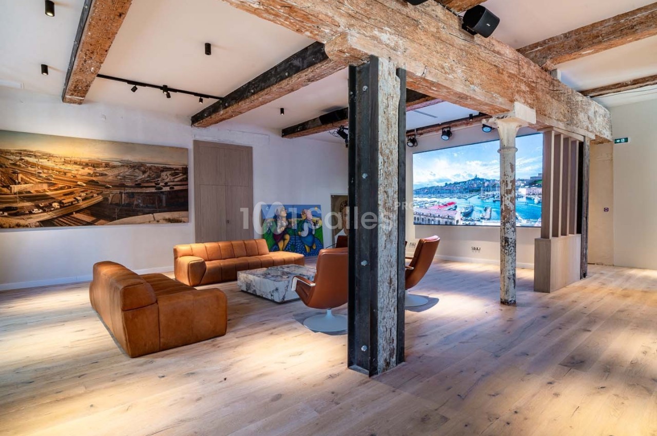Salle lumineuse avec poutres en bois apparentes, mobilier moderne et œuvres d'art accrochées aux murs.