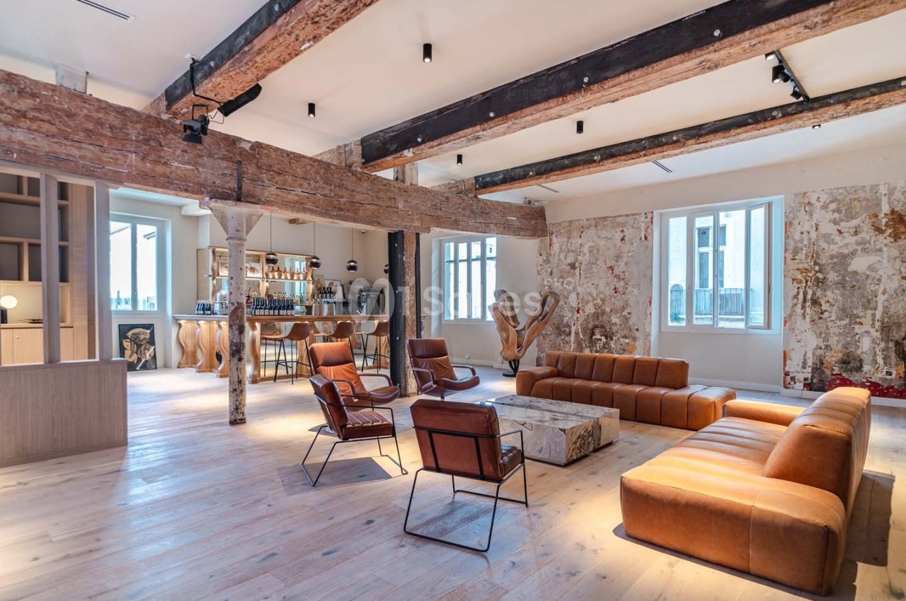 Espace intérieur lumineux avec poutres apparentes, murs texturés, mobilier en cuir et coin bar moderne.
