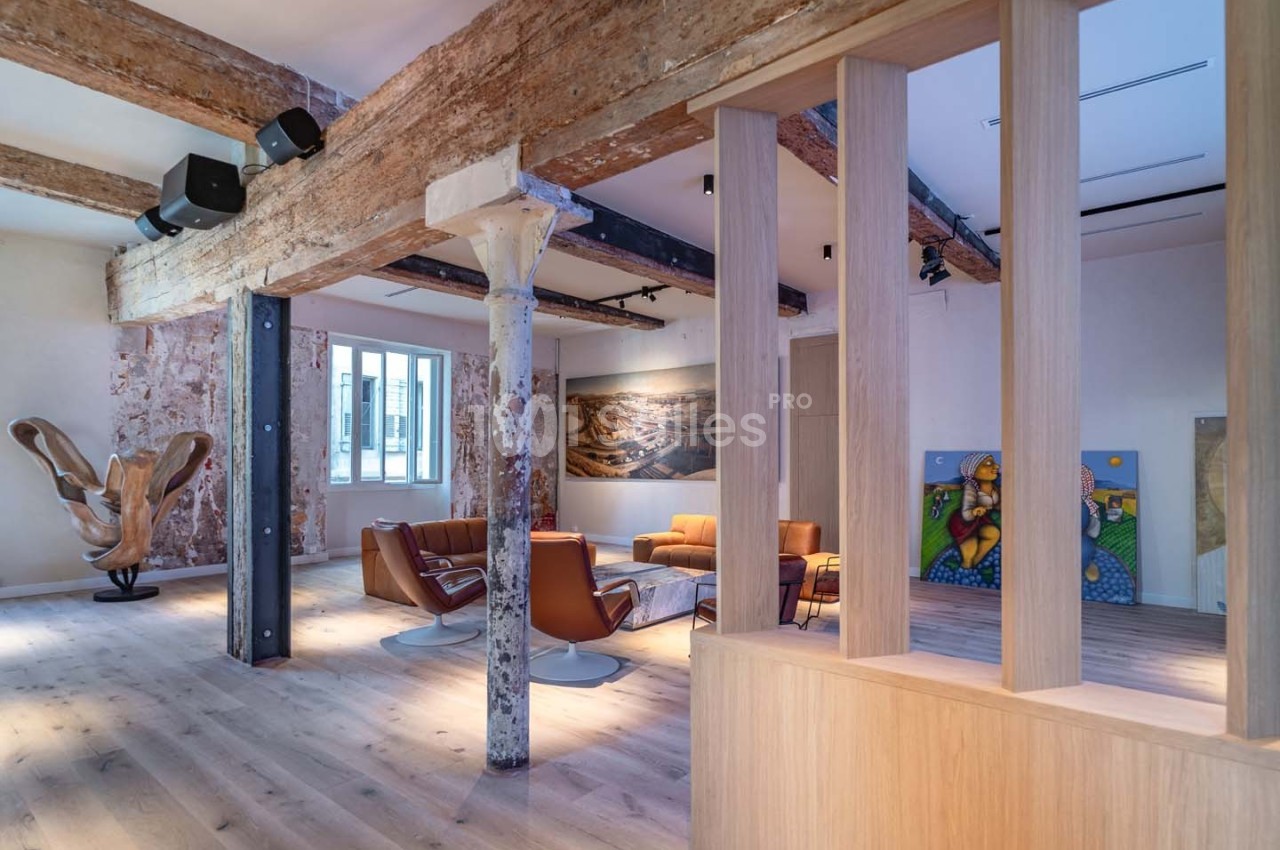 Espace intérieur lumineux avec poutres apparentes, mobilier moderne et œuvres d'art exposées sur les murs.