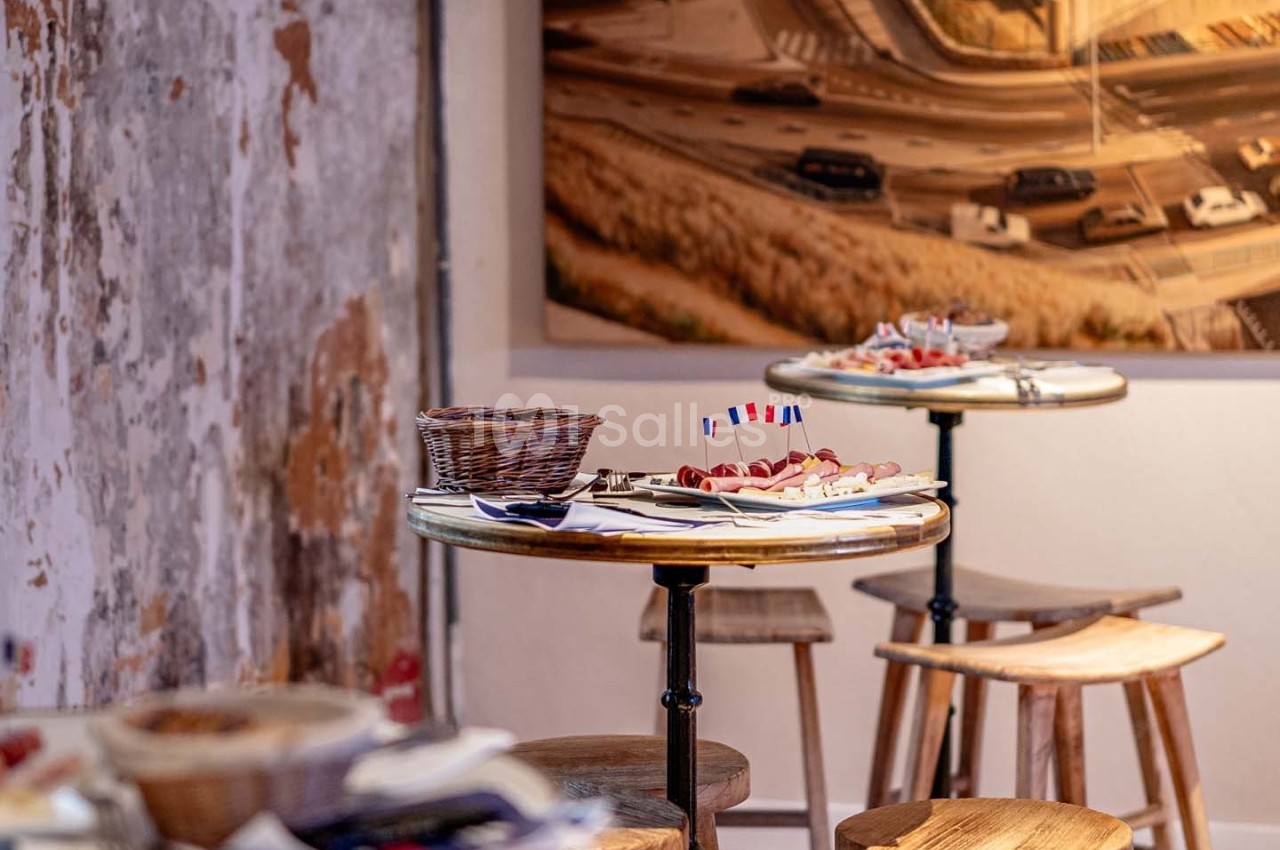Tables rondes en bois avec des assiettes de charcuterie et un décor mural urbain en arrière-plan.