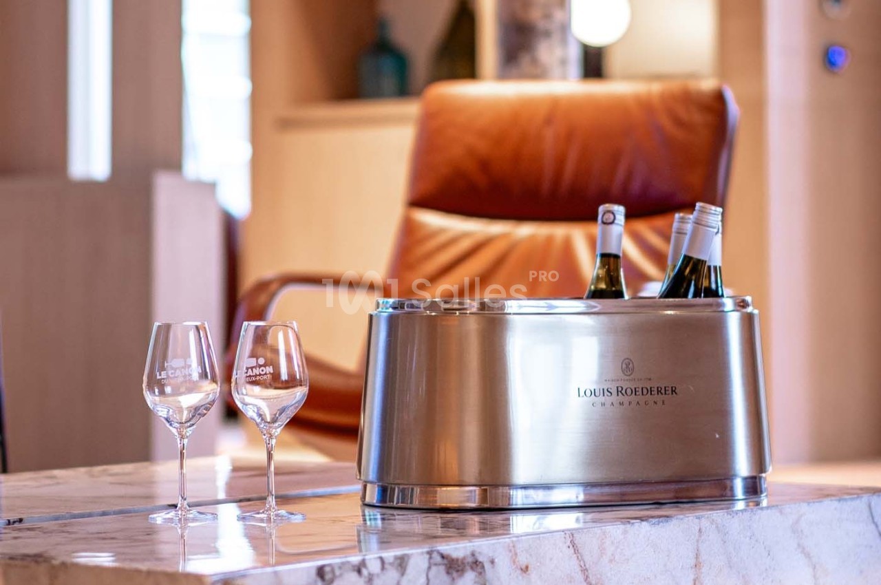 Seau à champagne avec bouteilles et deux verres sur une table en marbre, fauteuil en cuir en arrière-plan.