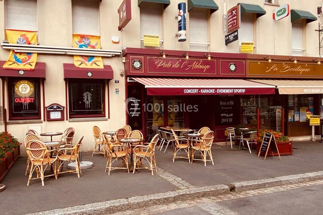 Terrasse avec chaises en osier devant un pub et une boutique, façade décorée de drapeaux et enseignes.