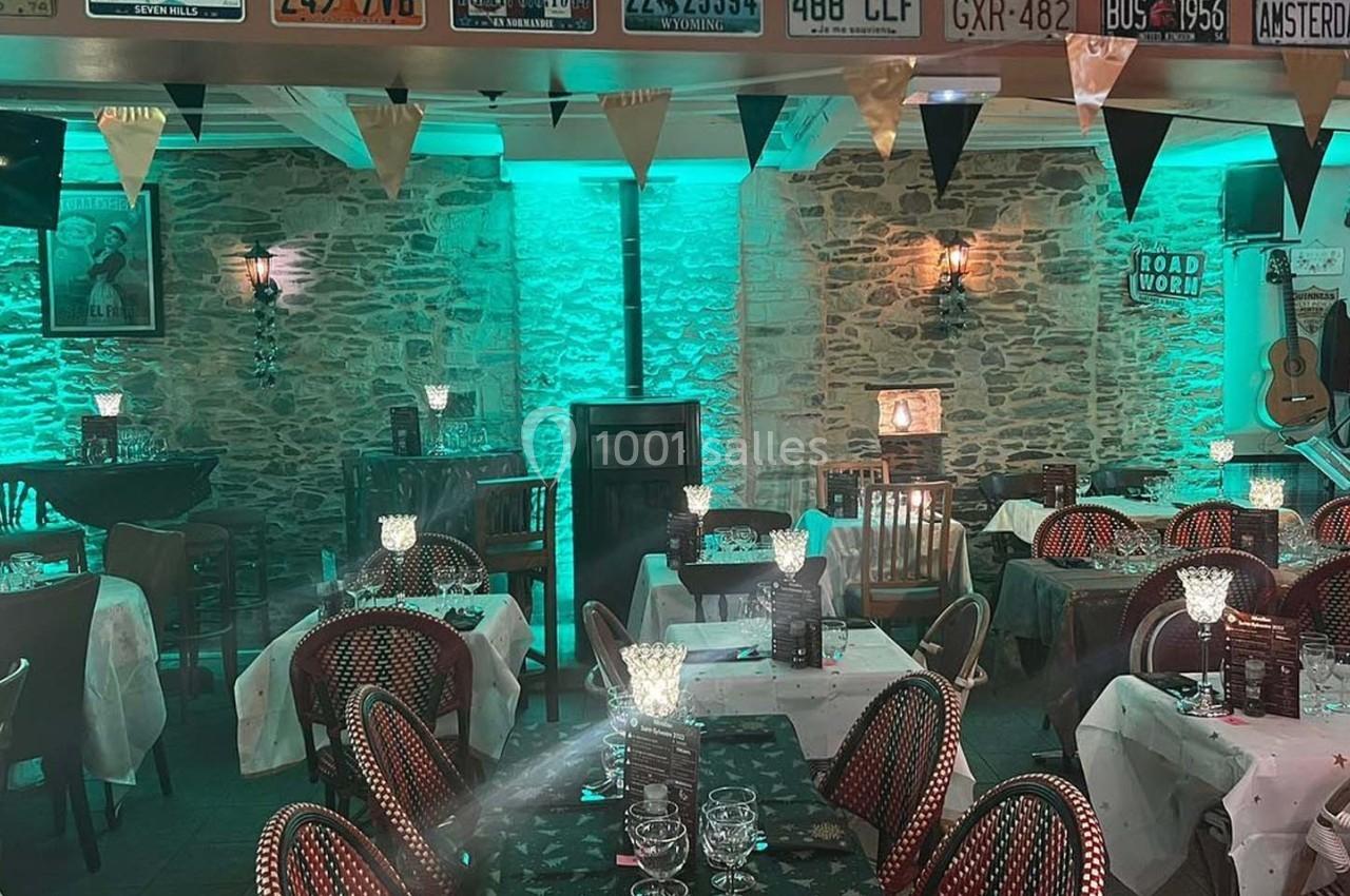 Salle de restaurant décorée avec des tables dressées, éclairage tamisé vert et murs en pierre apparente.