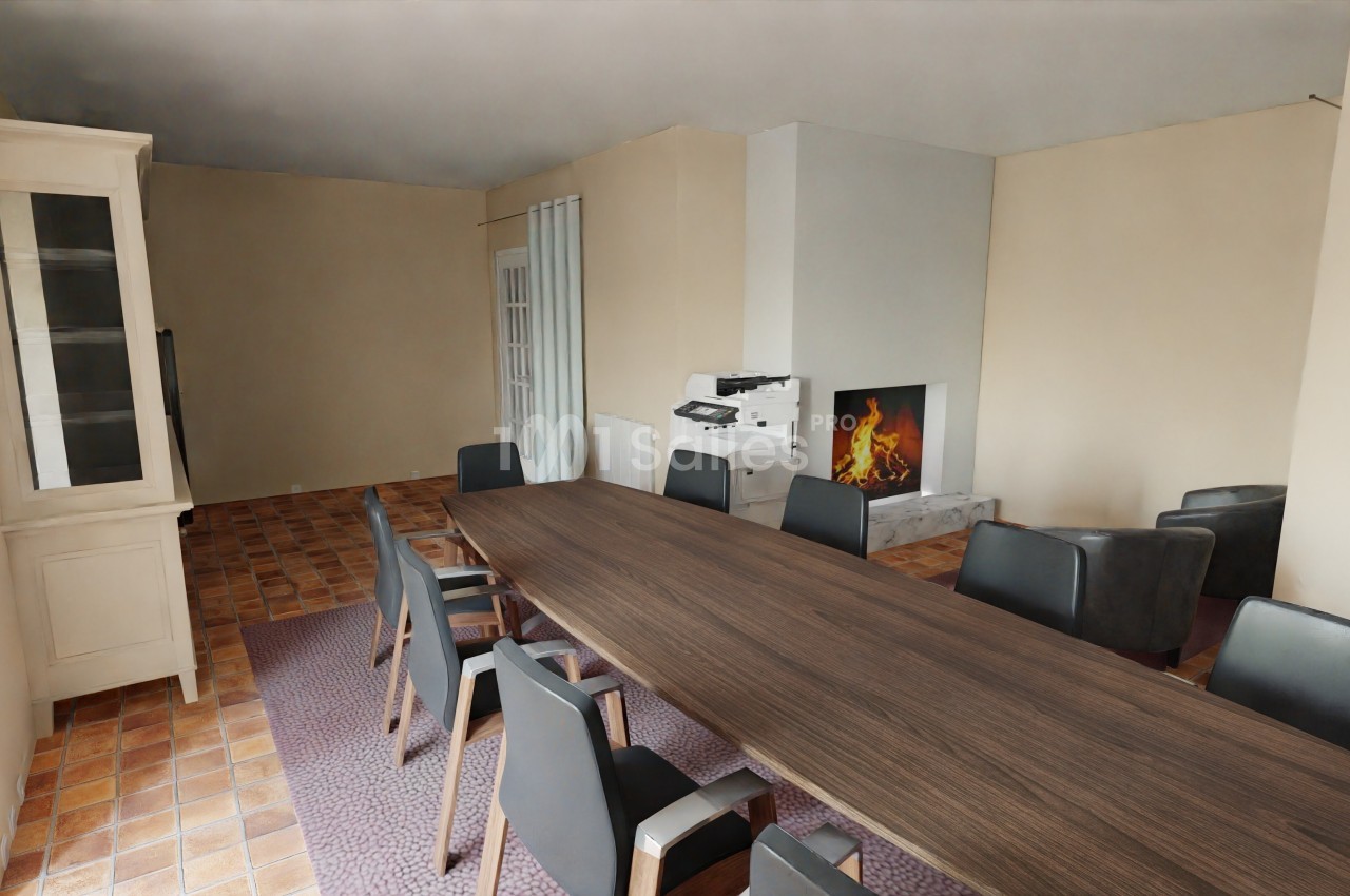 Salle de réunion avec grande table en bois, chaises noires, cheminée allumée et sol en carrelage.