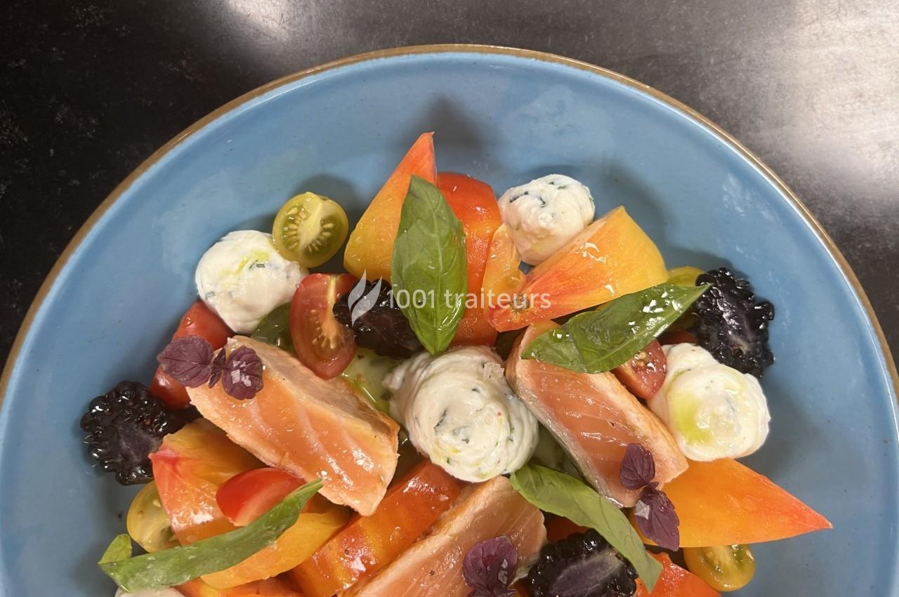 Assiette colorée de saumon fumé, tomates variées, mûres, herbes fraîches et quenelles de fromage sur une assiette bleue.