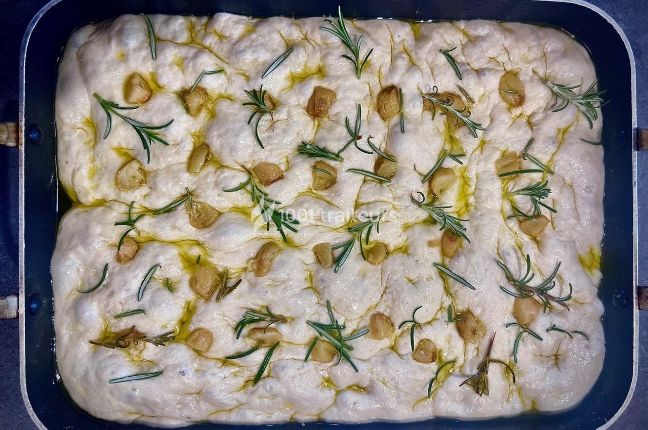 Pâte à focaccia crue garnie de romarin, d'ail et d'huile d'olive dans un moule rectangulaire.