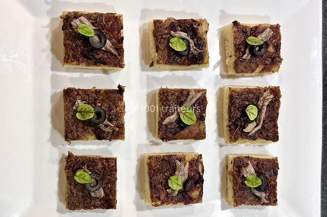 Carrés de pissaladière garnis d'oignons confits, olives noires, anchois et feuilles de basilic, disposés sur un plateau…