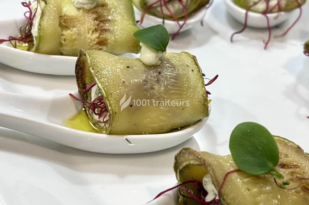 Rouleaux de courgettes grillées garnis de fromage frais et micro-pousses, présentés sur des cuillères en porcelaine blanche.