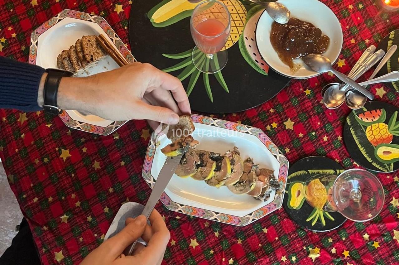 Une personne tartine une tranche de pain avec du foie gras sur une table décorée pour les fêtes.