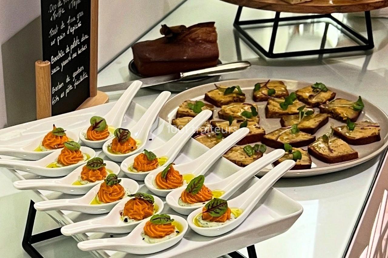Cuillères apéritives garnies de mousse orange et herbes fraîches, accompagnées de toasts sur un plateau.