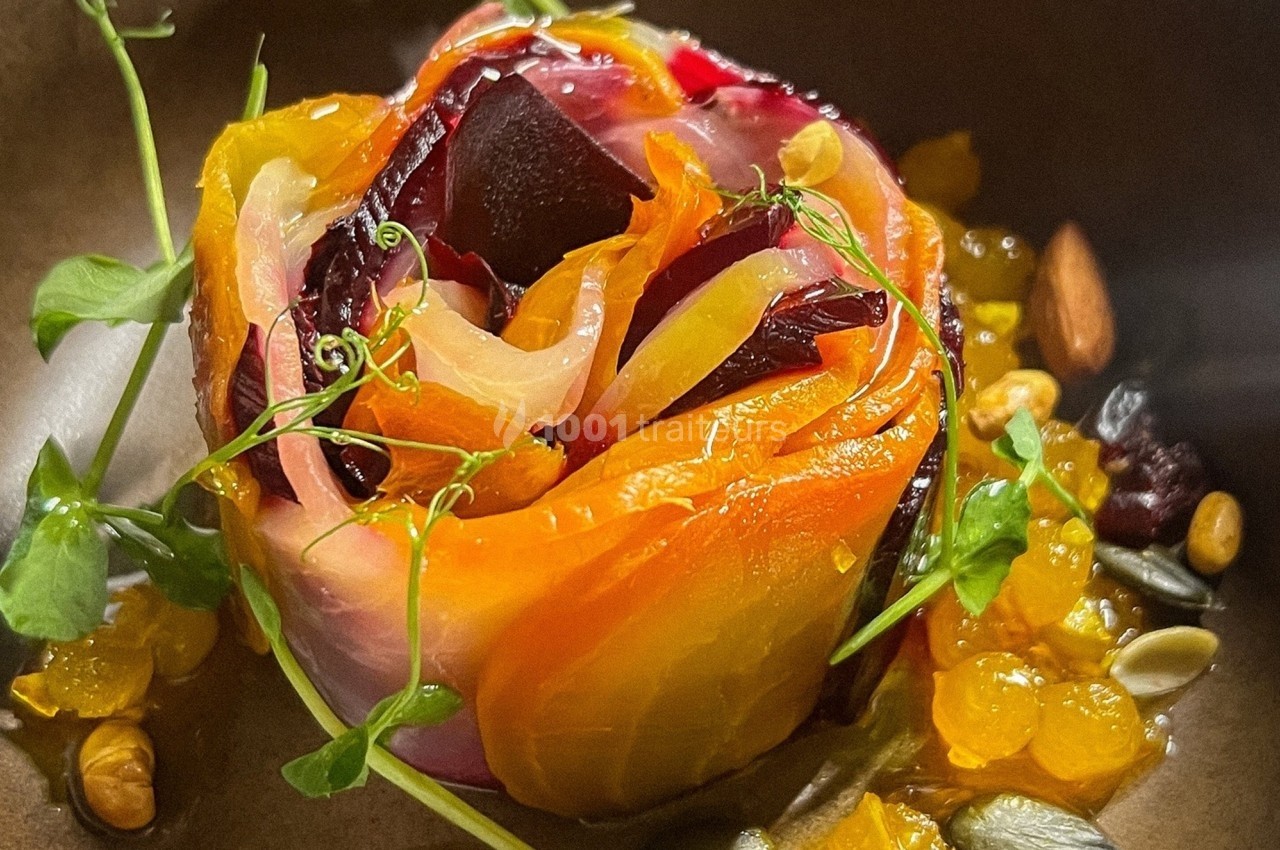 Assiette contenant une rose comestible composée de légumes colorés, garnie de graines, herbes fraîches et éclats dorés.