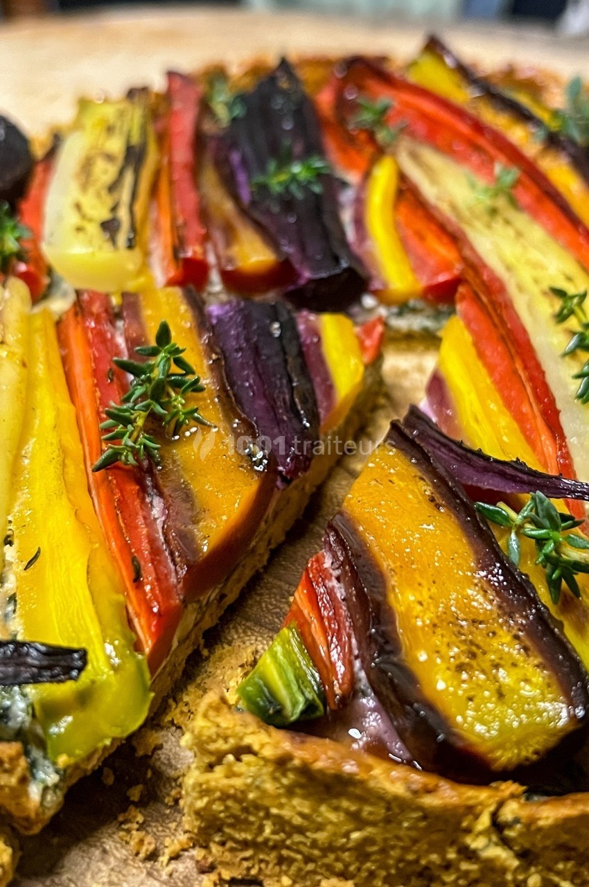 Tarte colorée garnie de légumes rôtis en tranches fines, décorée de brins de thym frais.