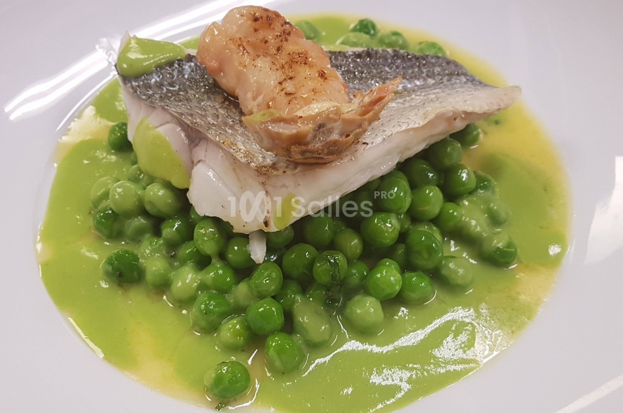 Filet de poisson avec peau grillée, posé sur des petits pois et une sauce verte, garni d'une langoustine.