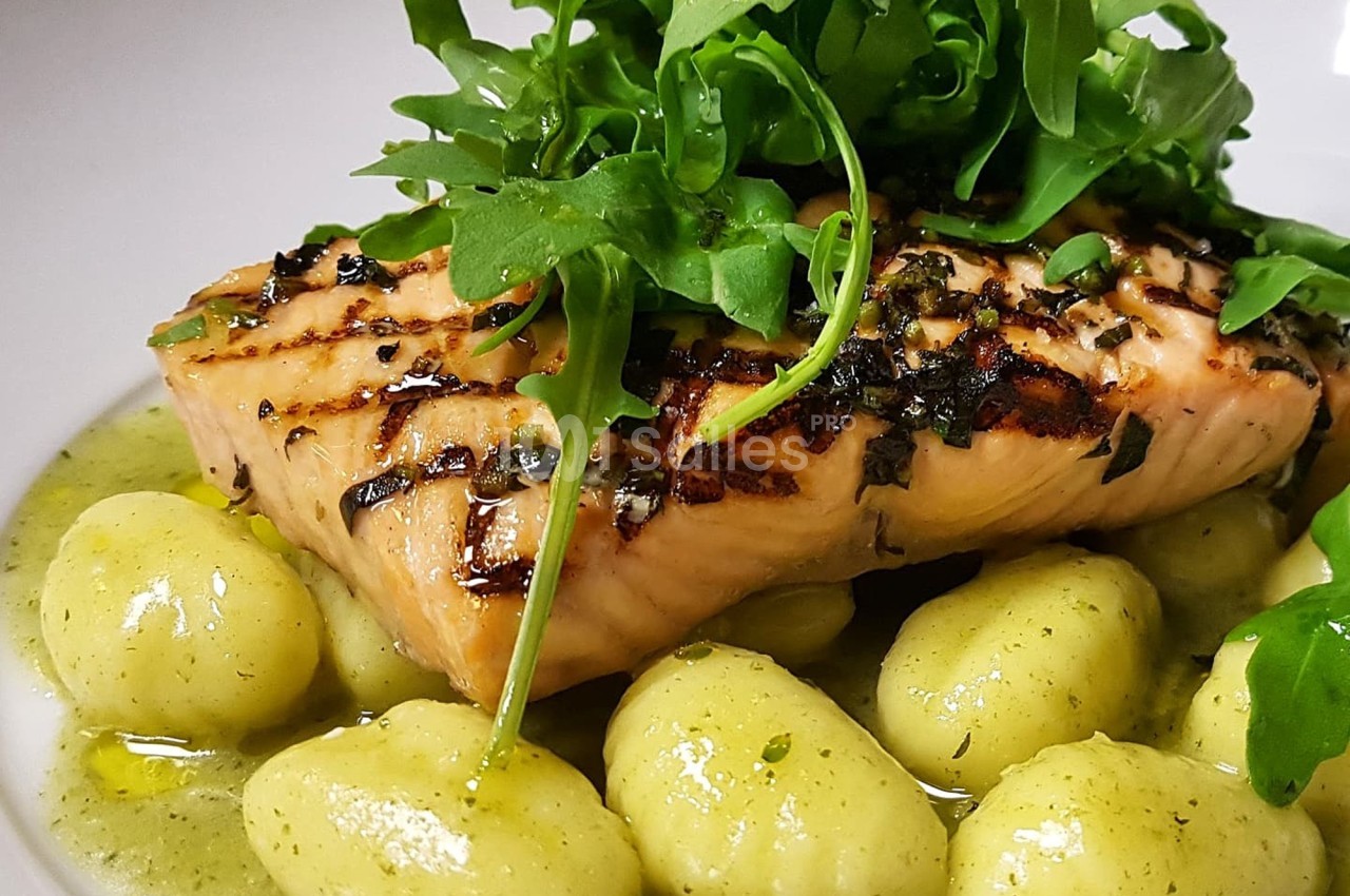 Filet de saumon grillé sur lit de gnocchis nappés de sauce verte, garni de roquette fraîche.