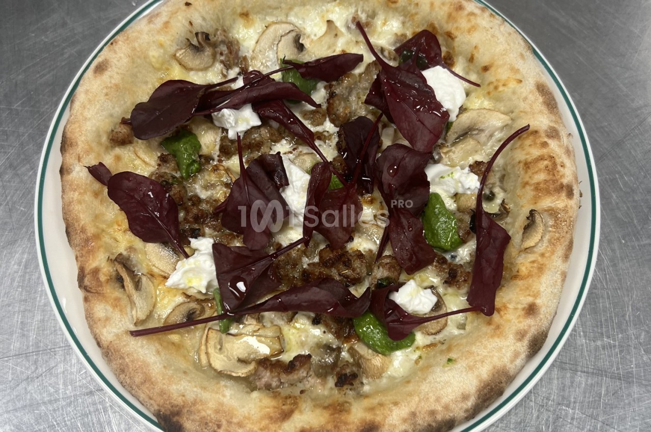 Pizza garnie de champignons, fromage frais, feuilles rouges et herbes, servie sur une assiette blanche.