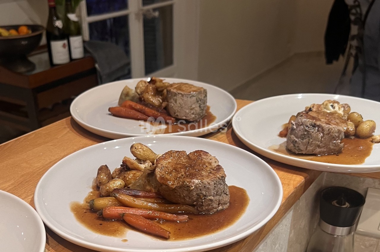 Assiettes de filet de viande servi avec carottes, pommes de terre rôties et sauce, disposées sur un comptoir en bois.