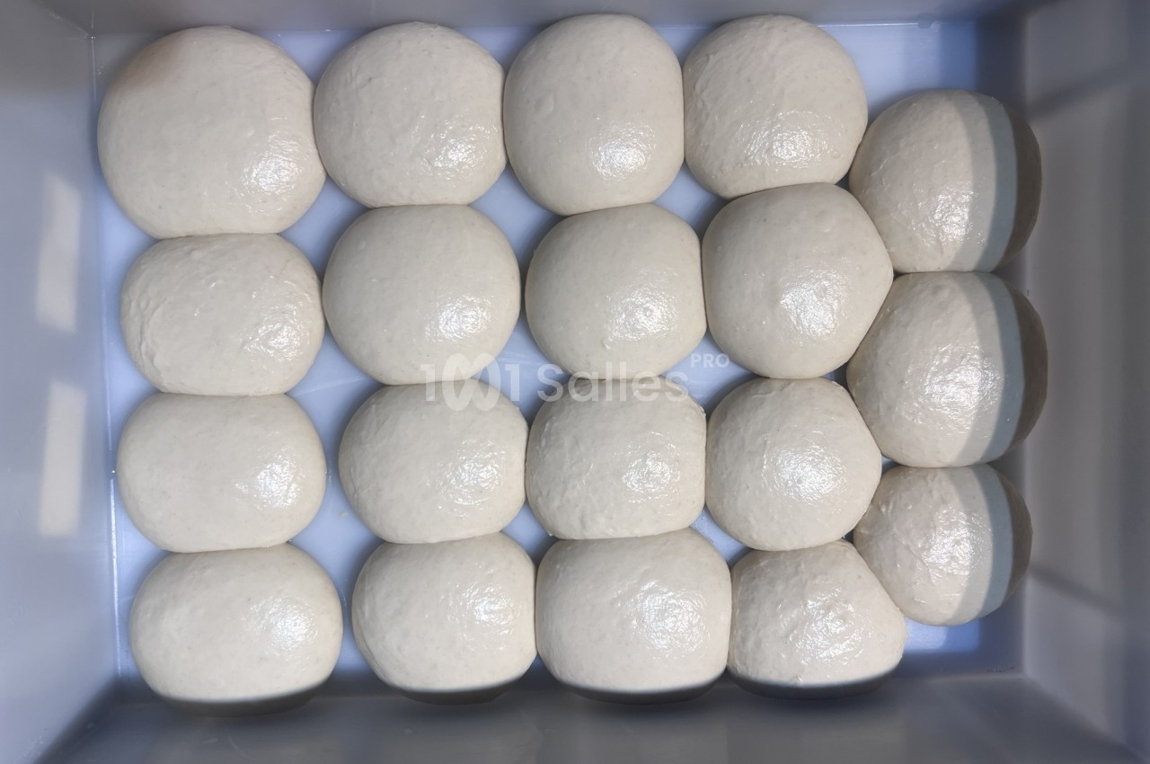 Boules de pâte crue alignées en rangées dans un bac rectangulaire.
