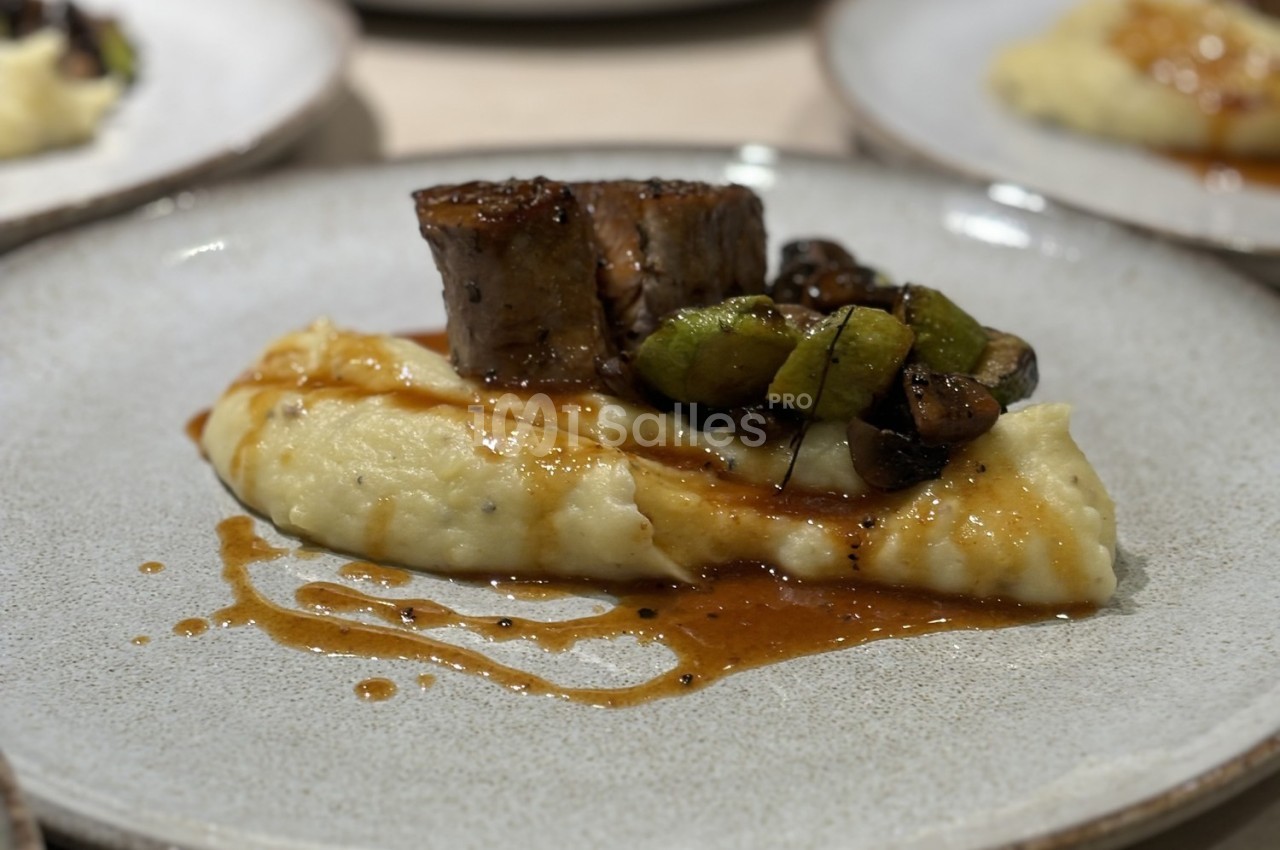 Assiette contenant une purée crémeuse garnie de viande, légumes verts et champignons avec une sauce.