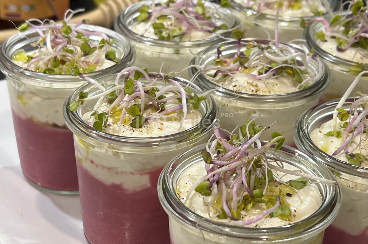 Verrines de mousse rose surmontées de crème blanche, graines germées et éclats de pistaches.