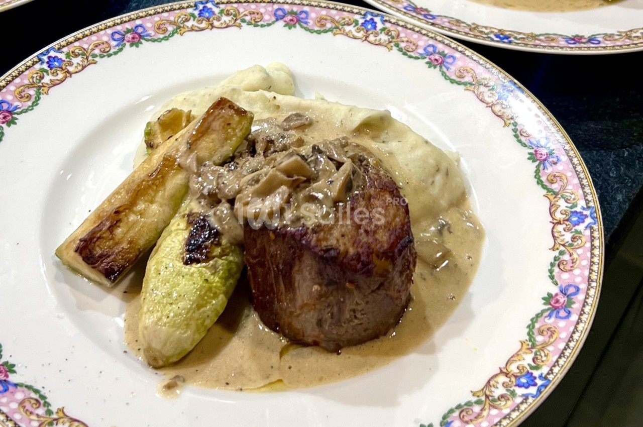 Assiette contenant un filet de viande avec sauce, purée de pommes de terre et légumes grillés, servie sur une vaisselle…