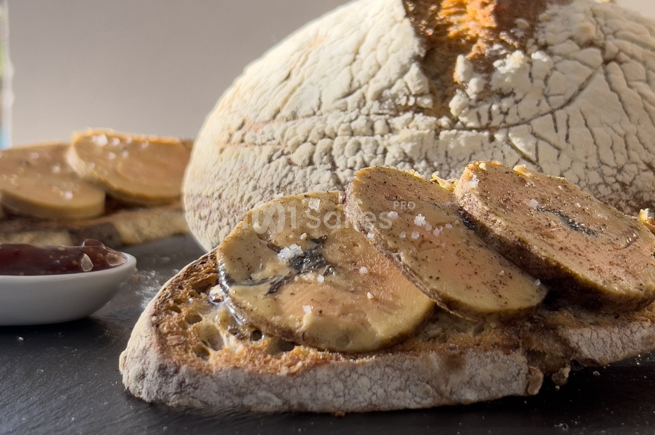 Tranche de pain grillé garnie de foie gras, accompagnée d'une miche de pain et d'une coupelle de confiture.
