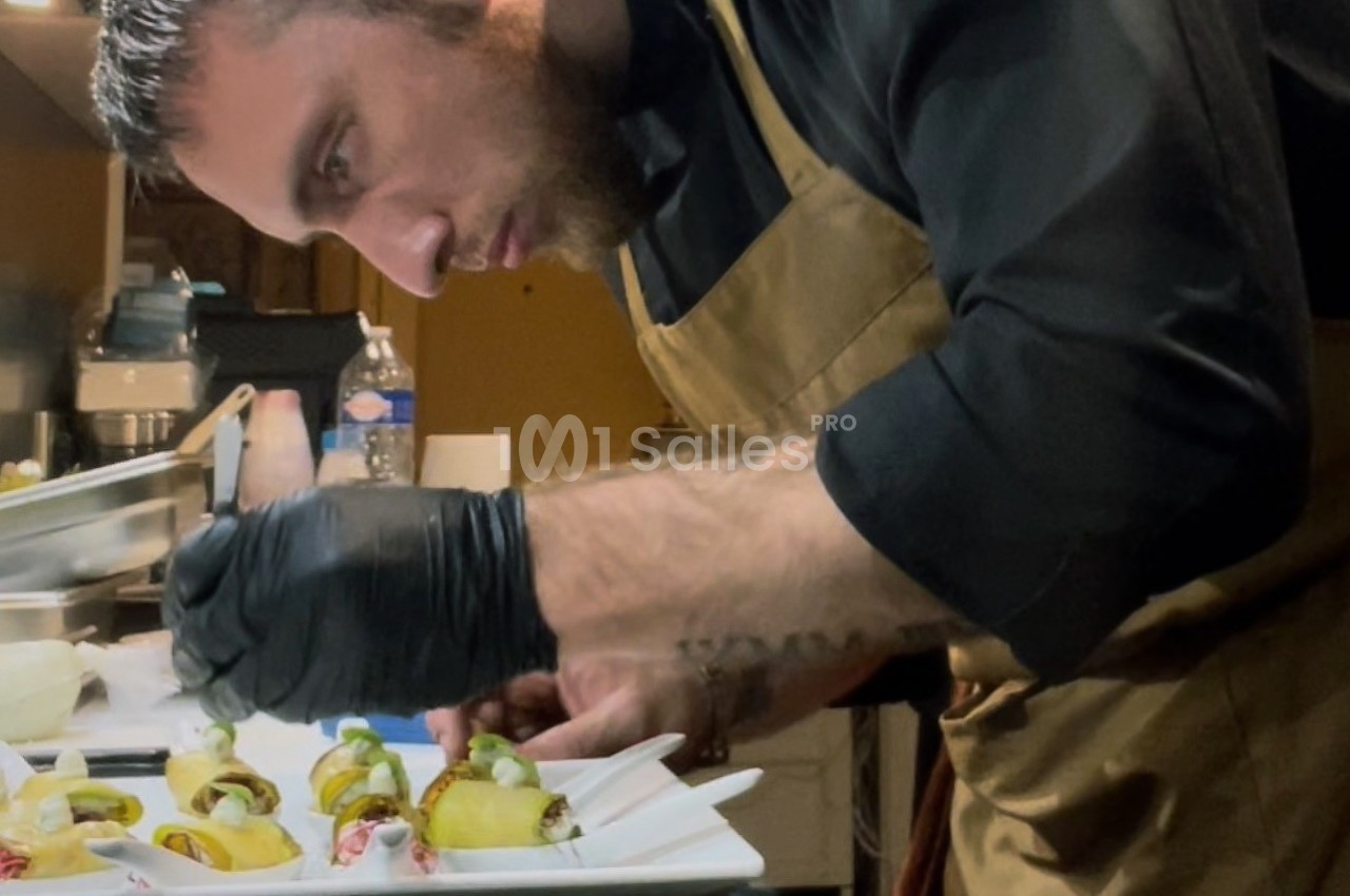 Un chef en tablier prépare soigneusement des plats gastronomiques dans une cuisine professionnelle.