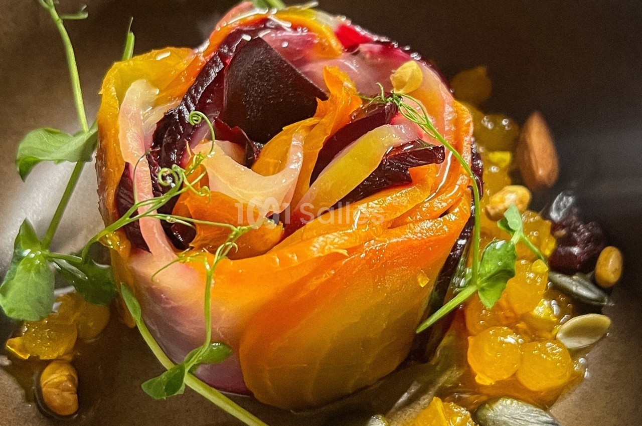 Assiette contenant une rose comestible faite de légumes colorés, garnie de graines, herbes fraîches et condiments.