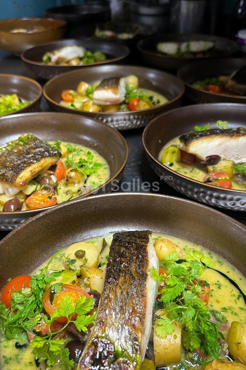 Assiettes de poisson grillé servies avec légumes, pommes de terre, herbes fraîches et sauce crémeuse.