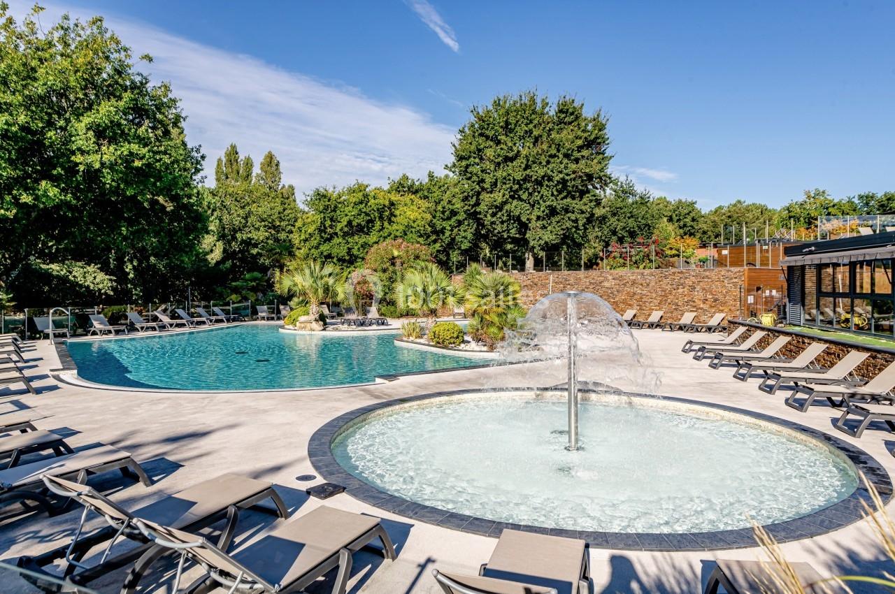 Piscine extérieure avec bassin principal, pataugeoire avec fontaine, transats et végétation environnante.