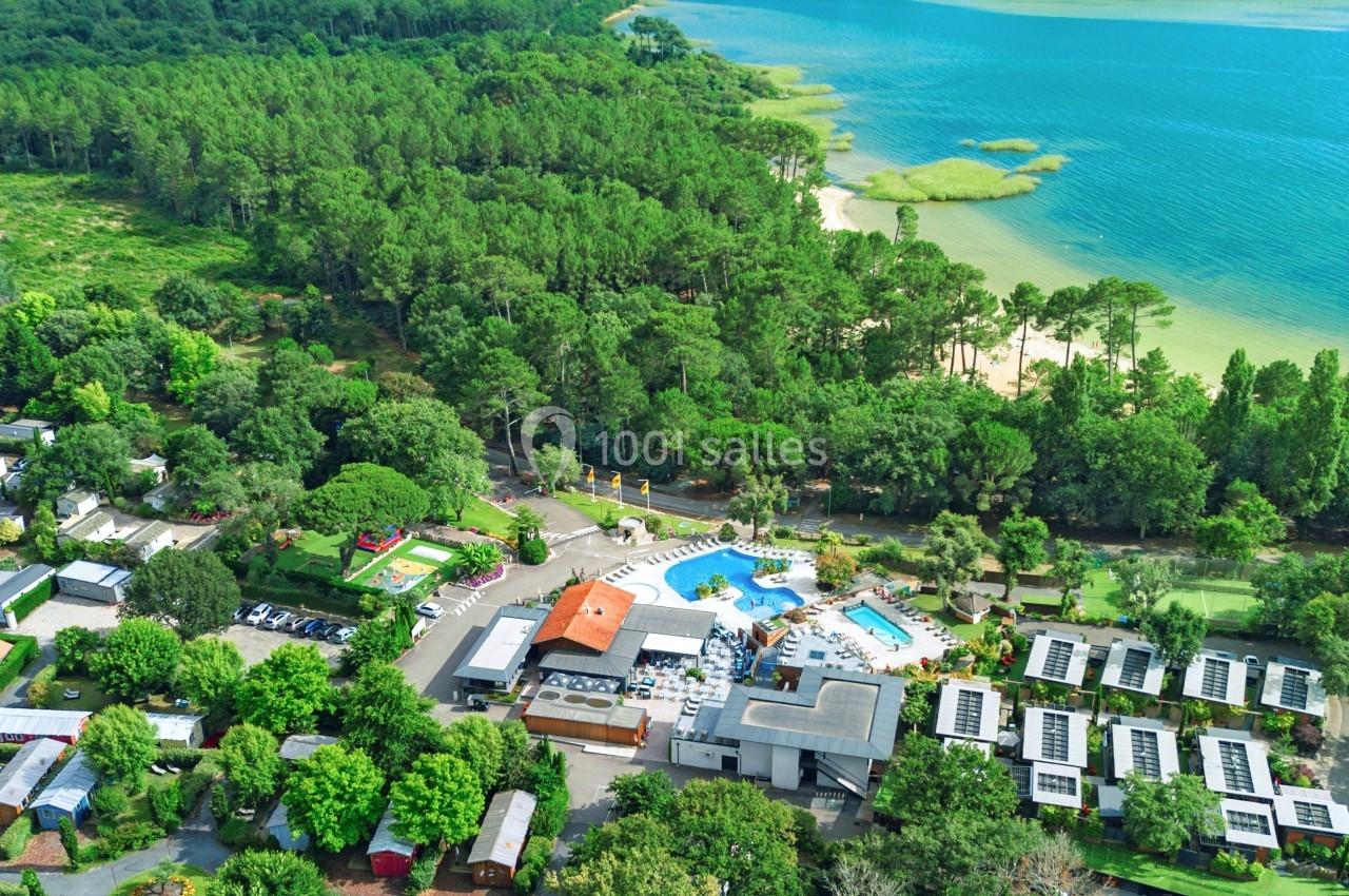 Vue aérienne d'un camping entouré de forêt, avec piscine et accès à un lac bordé de végétation.